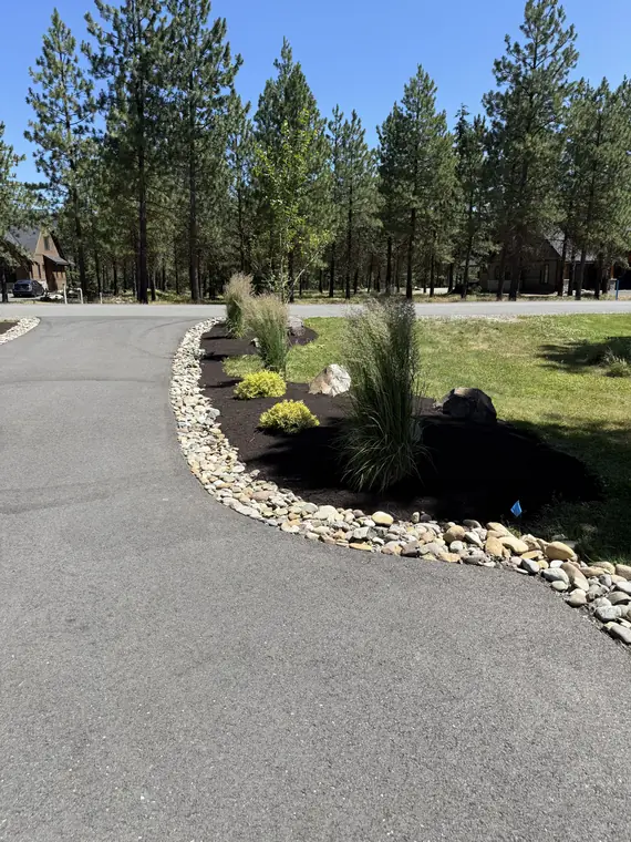 Planted bed with a river-rock border curving along a paved drive
