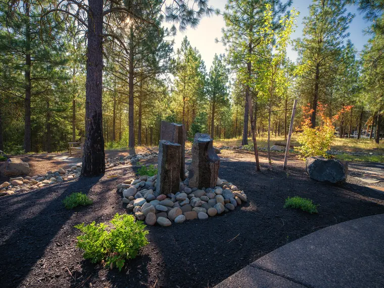 Bubbling stone-column water feature ringed with river rock under pines