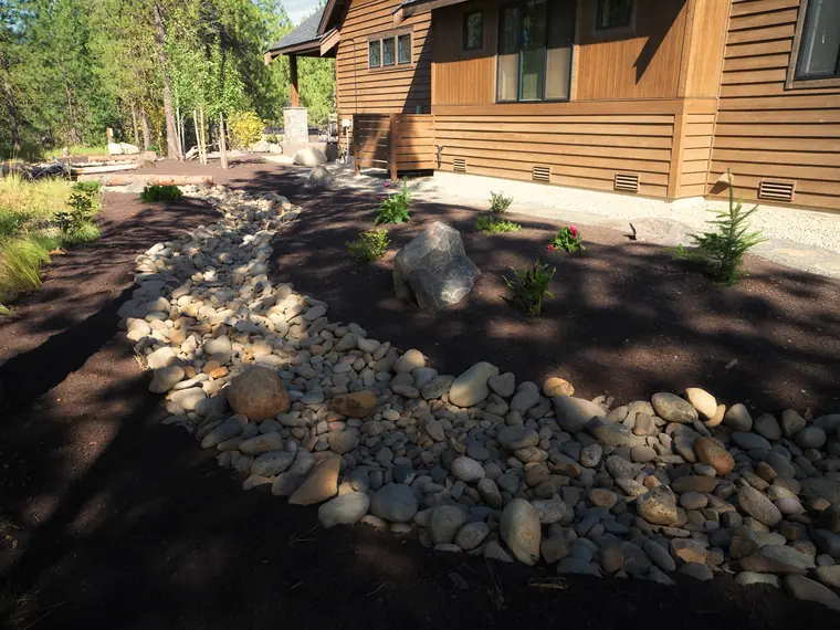 River-rock creek bed curving past a boulder beside the home