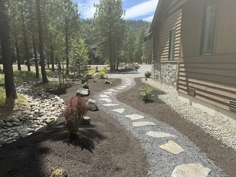 Flagstone walkway set in gravel between planting beds beside a timber home