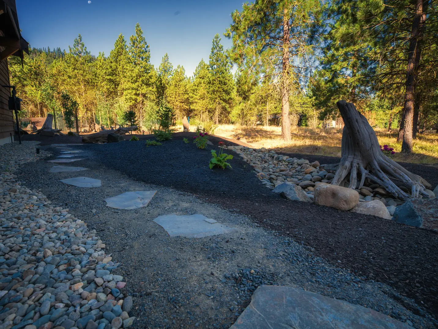 Flagstone stepping-stone path winding through river rock and dark mulch beds under pines