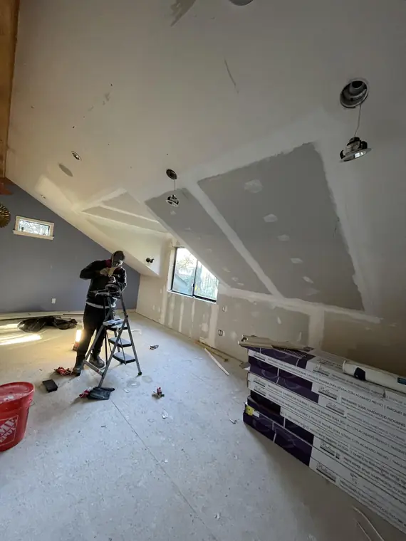 Vaulted room mid-refresh, with ceiling repairs under way and boxes of new flooring staged by the wall