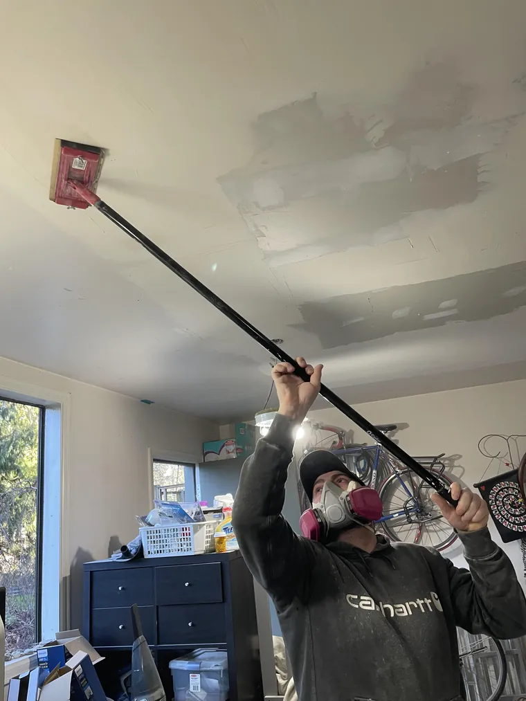 Sanding a patched ceiling smooth with a pole sander before paint