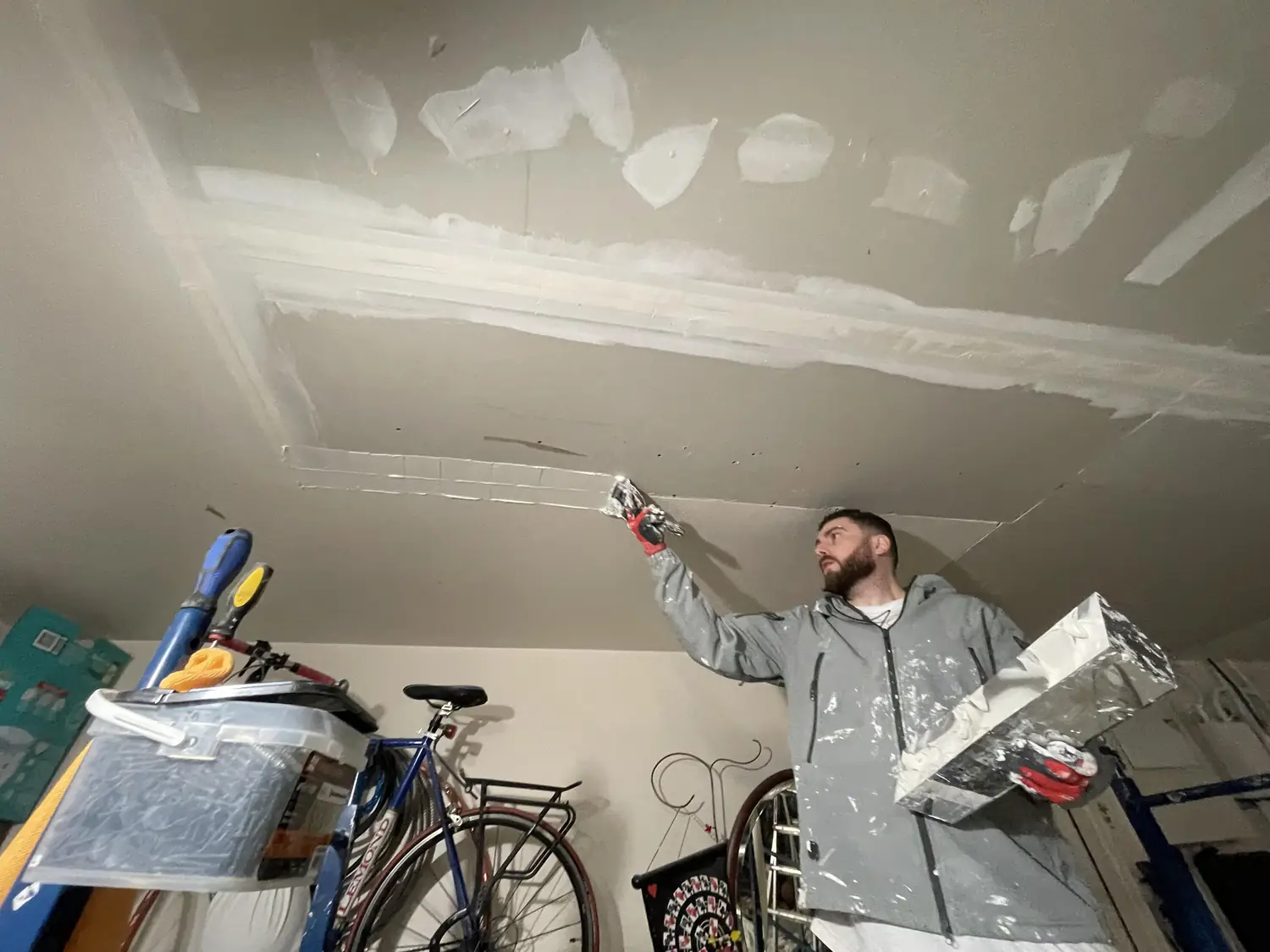 Crew member applying joint compound to a drywall ceiling repair
