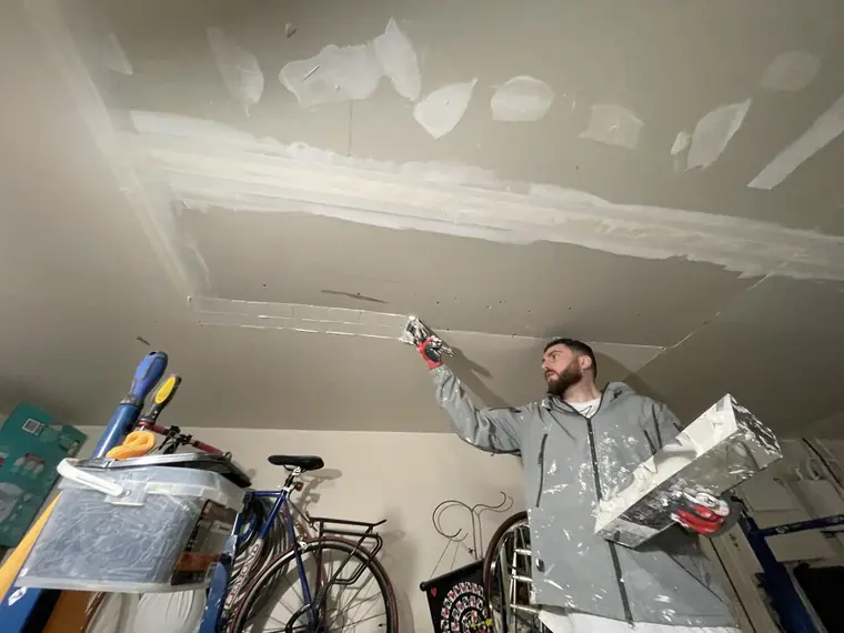 Crew member applying joint compound to a drywall ceiling repair