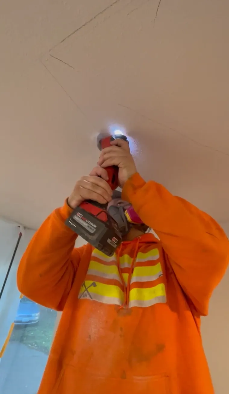 Crew member installing a new ceiling fixture with a drill