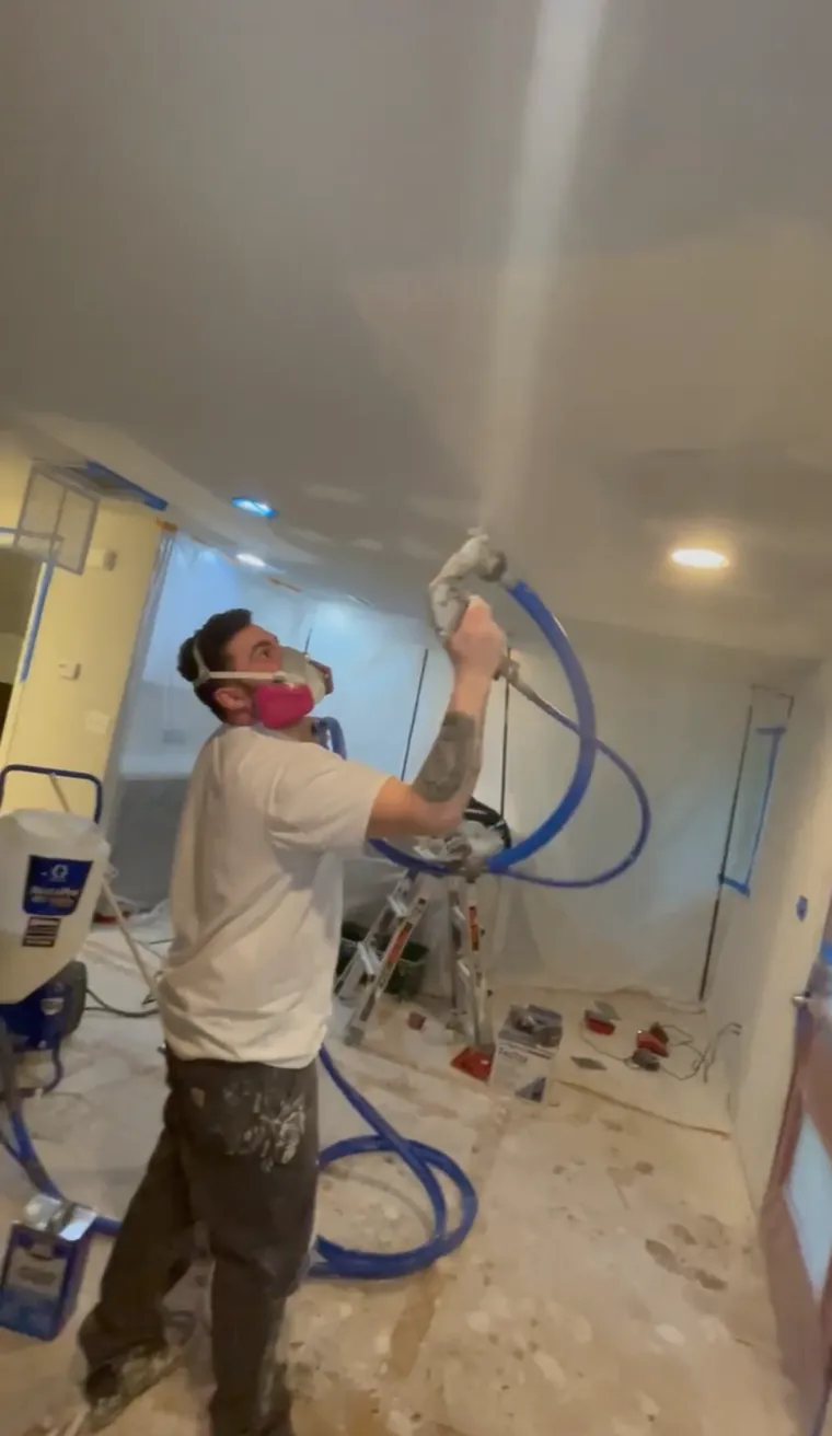 Spraying new ceiling texture over a repaired ceiling in a masked-off room