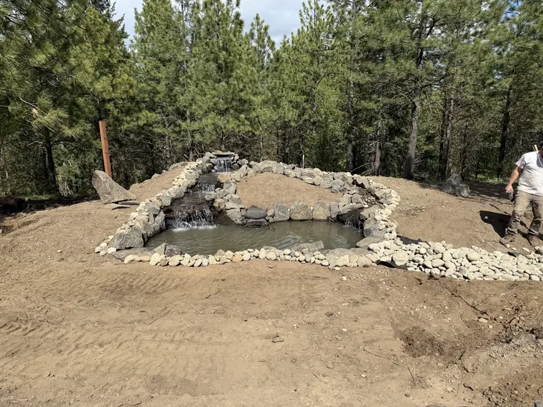 Pond basin shaped and edged with stone on freshly graded ground in May