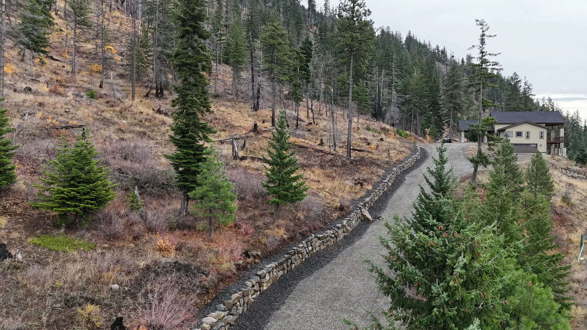 Aerial view of a long boulder rockery climbing beside a steep gravel driveway below a mountain home