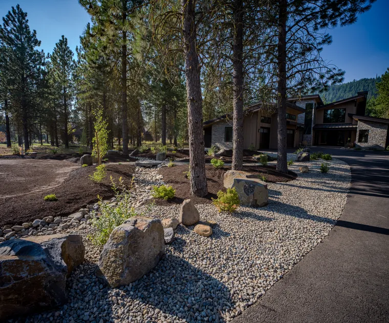 Boulders and river rock in a bed beside the driveway, under tall pines