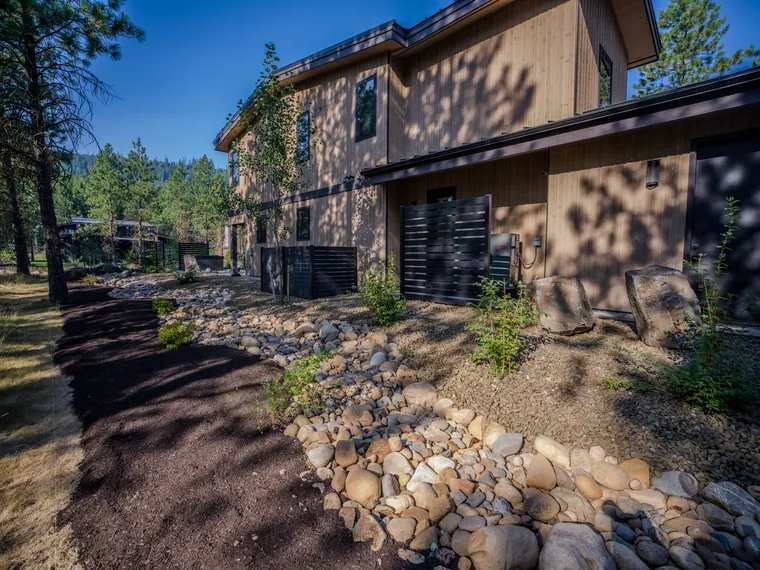 Dry creek with boulders and young plantings along the side of the house