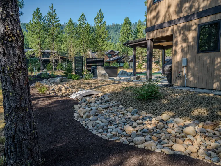 River-rock dry creek bed with a small footbridge, leading toward the covered back patio of a new home at Tumble Creek