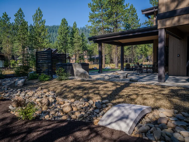 Small footbridge over a river-rock dry creek beside a covered patio