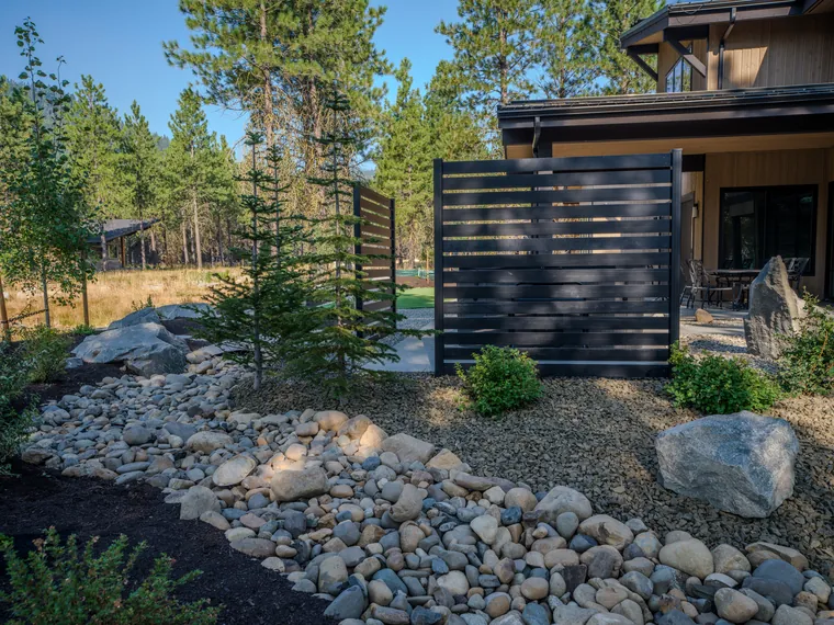 Dry creek, boulders and a young spruce in the side yard
