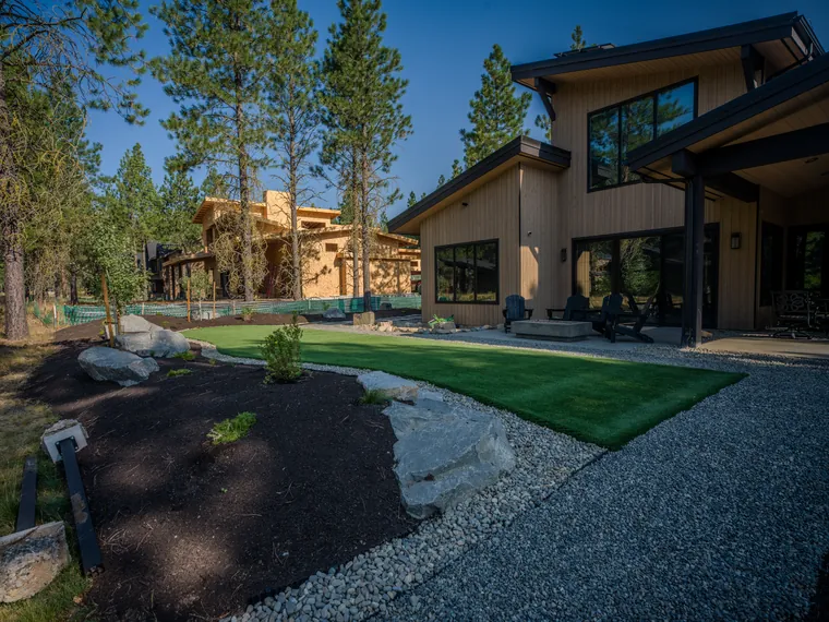 Artificial turf edged with a gravel path and boulder beds behind the home