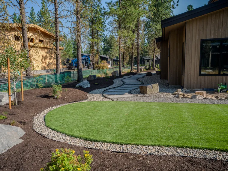 Curved artificial turf ringed with river rock, with a flagstone stepping path, at a Tumble Creek home