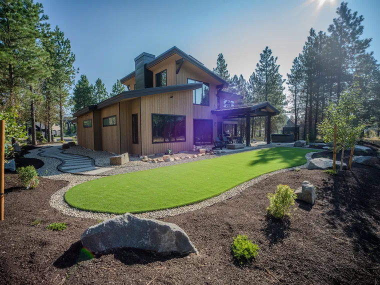 Artificial turf bordered by mulch beds and boulders at a Tumble Creek home
