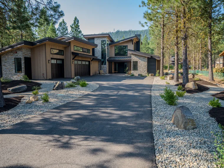 Driveway approach framed by river-rock beds and boulders under pines