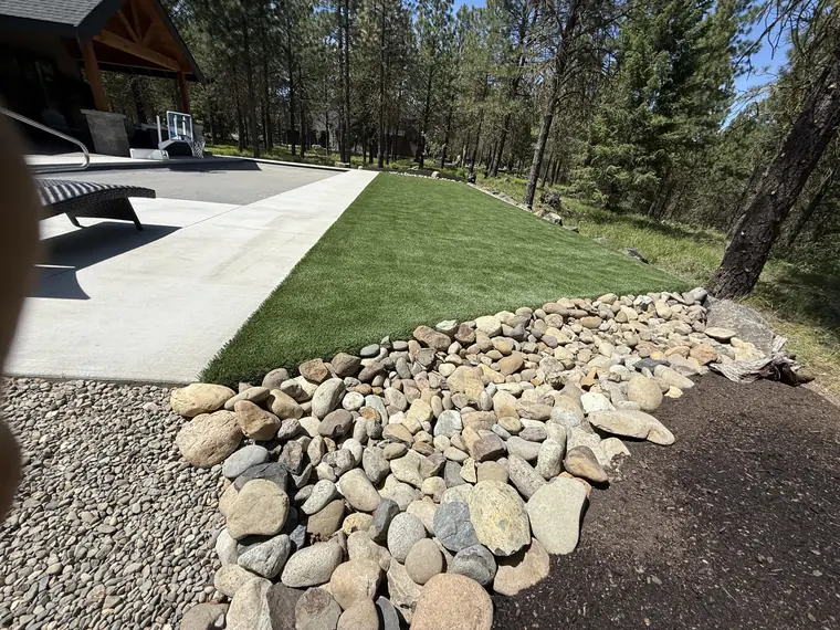 Synthetic turf meeting a river-rock border beside a patio