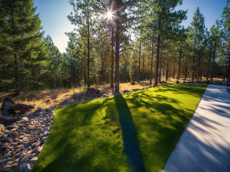 Artificial turf strip edged with river rock beside a concrete walk under pines in Suncadia