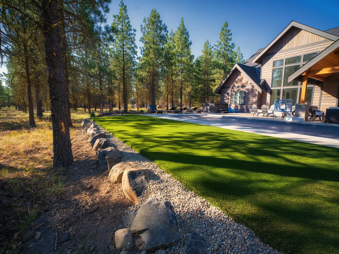 Artificial turf with a boulder and river-rock border beside a pool patio at a Suncadia home